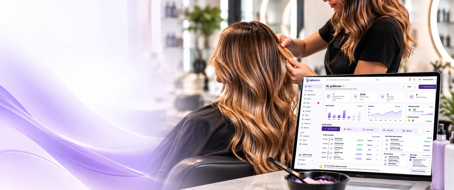 A stylist working on a client's long layered brown and blonde hair, next to a laptop showing the SalvaSalon dashboard with today's schedule
